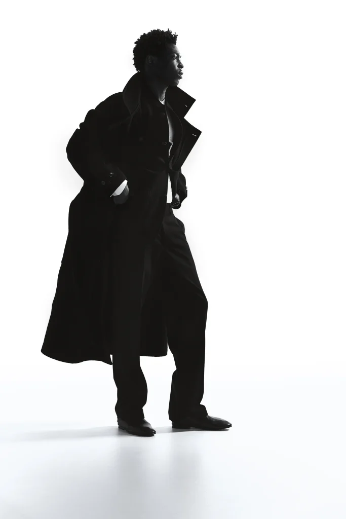 Model in lange zwarte wollen jas als silhouet tegen een witte achtergrond, Gogetti editorial