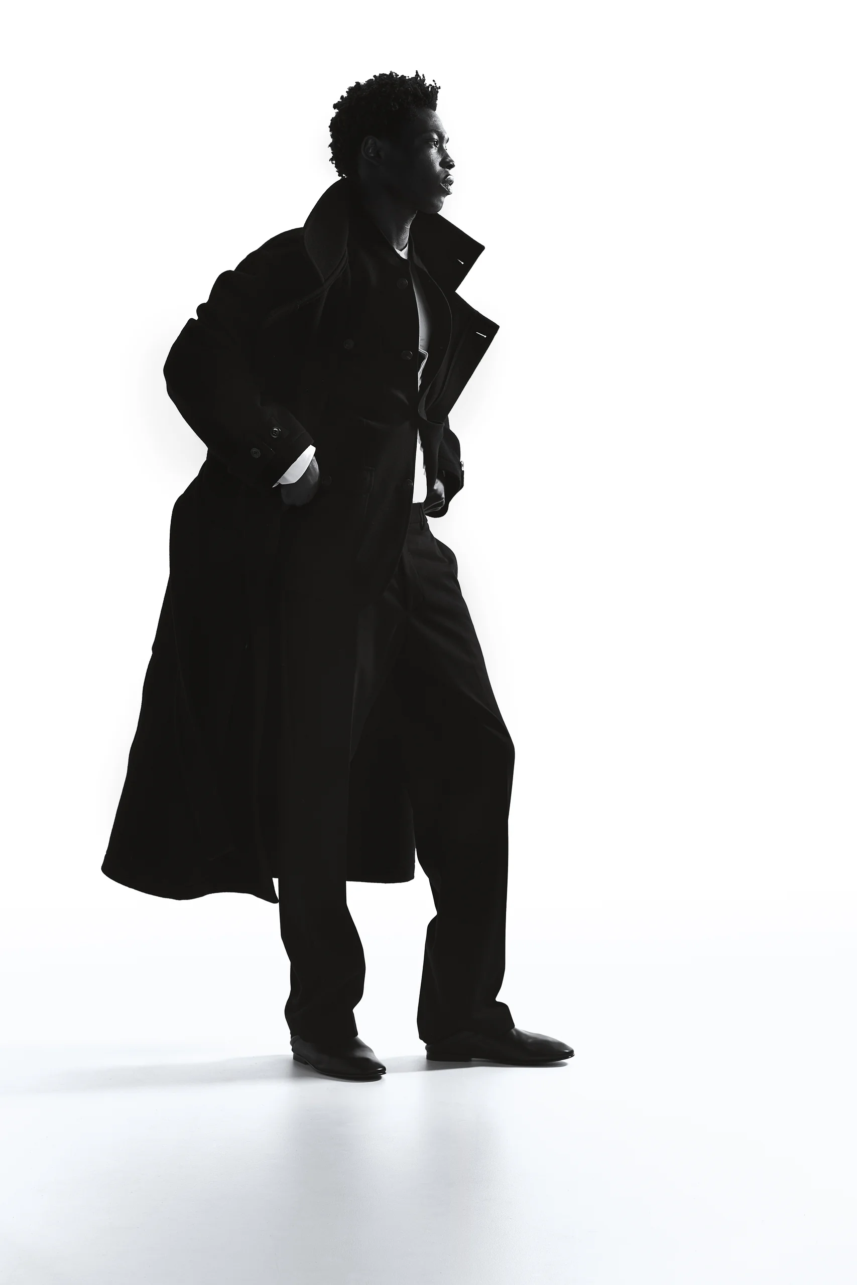 Model in lange zwarte wollen jas als silhouet tegen een witte achtergrond, Gogetti editorial
