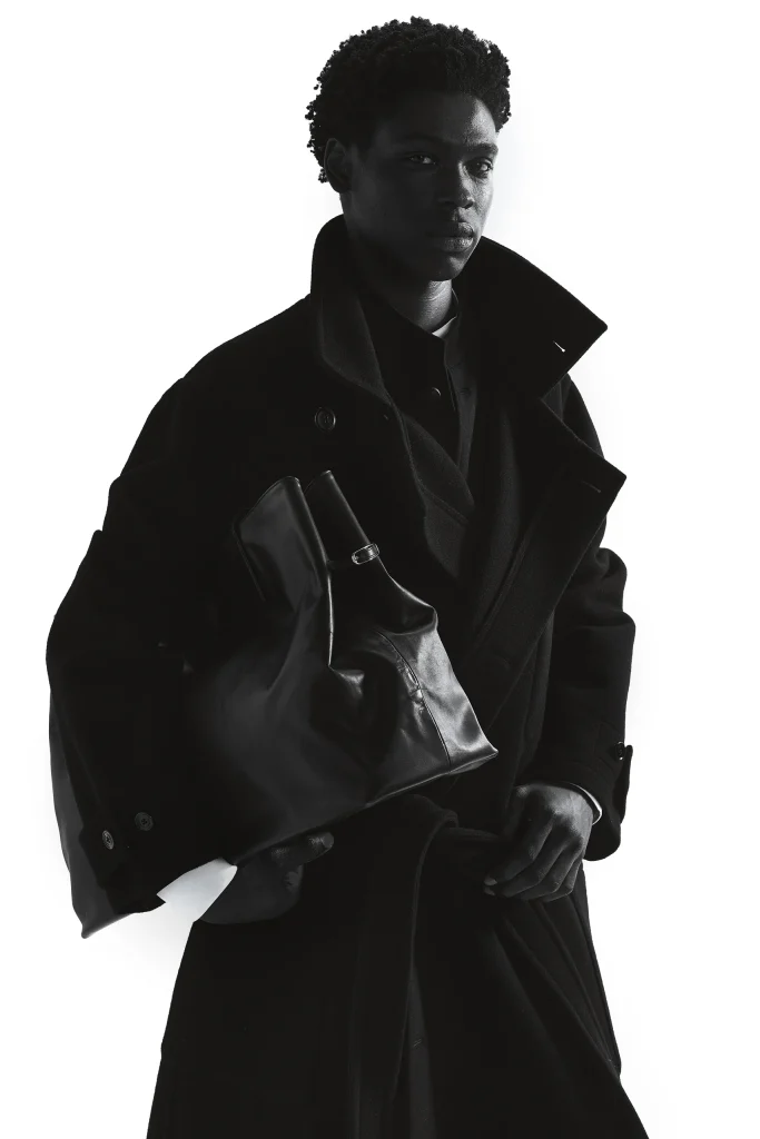 Model in oversized zwarte jas met een zwarte leren tas, Gogetti editorial