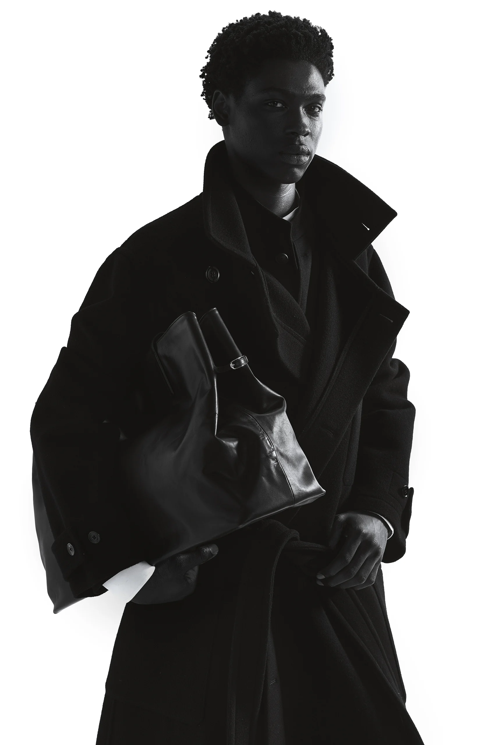 Model in oversized zwarte jas met een zwarte leren tas, Gogetti editorial